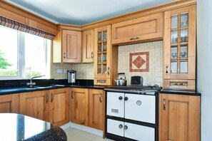 A kitchen with wooden cabinets, a black countertop, and a white stove. - Mannin Lodge (Ballyconneely)