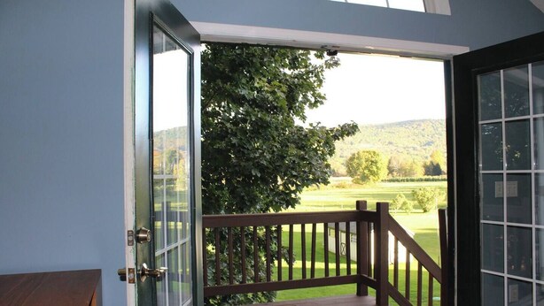 A wooden deck with a glass door leading to a view of a green landscape and hills. - Creekside Loft + Allstar Deluxe (Otego)