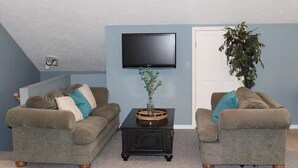 A living room with two grey sofas, a black coffee table, and a flat-screen TV on the wall. - Creekside Loft + Allstar Deluxe (Otego)