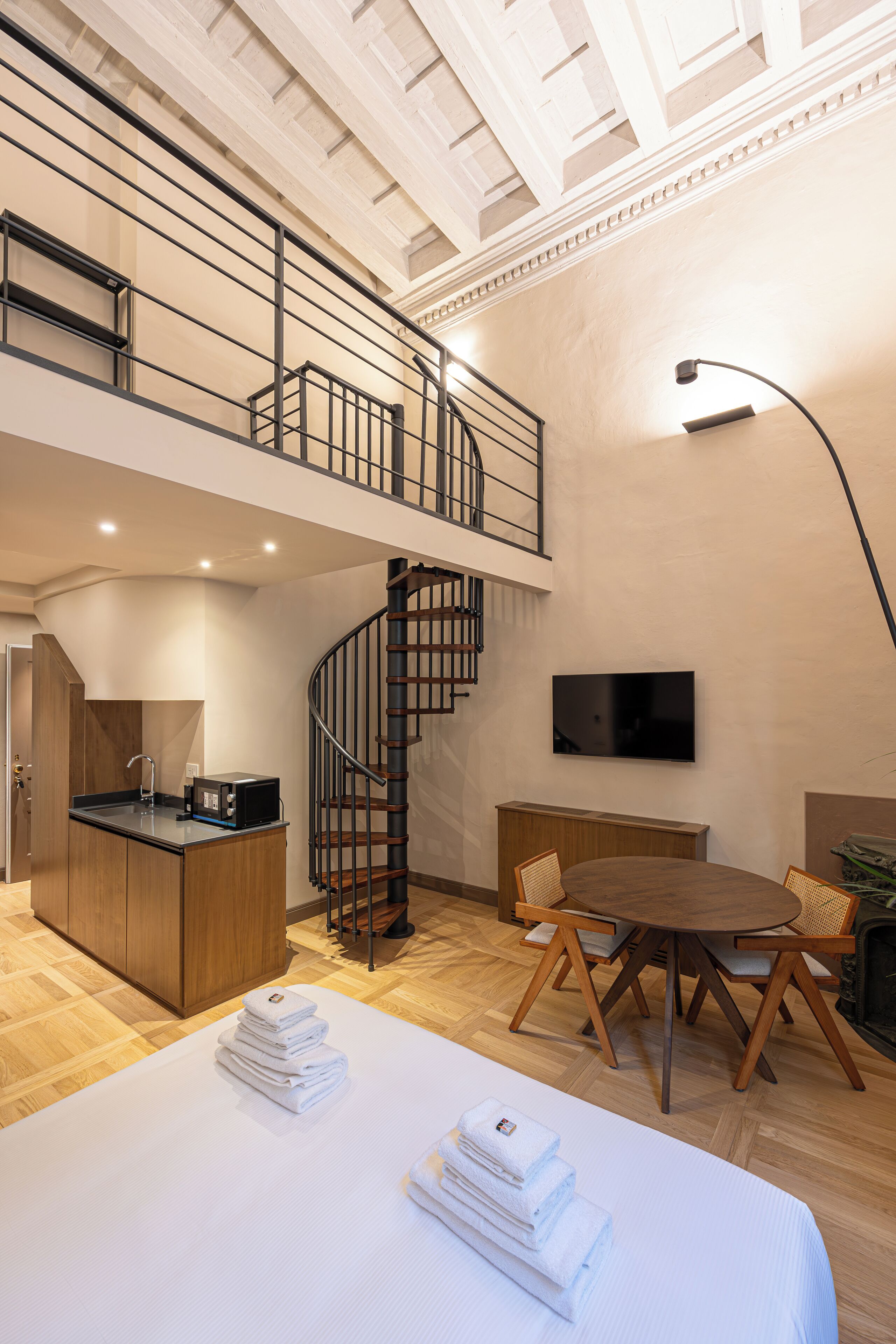 A spacious room with a large bed, a dining area, a kitchen, and a staircase leading to an upper level.