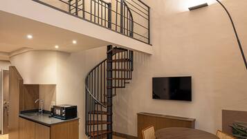 A spacious room with a large bed, a dining area, a kitchen, and a staircase leading to an upper level.