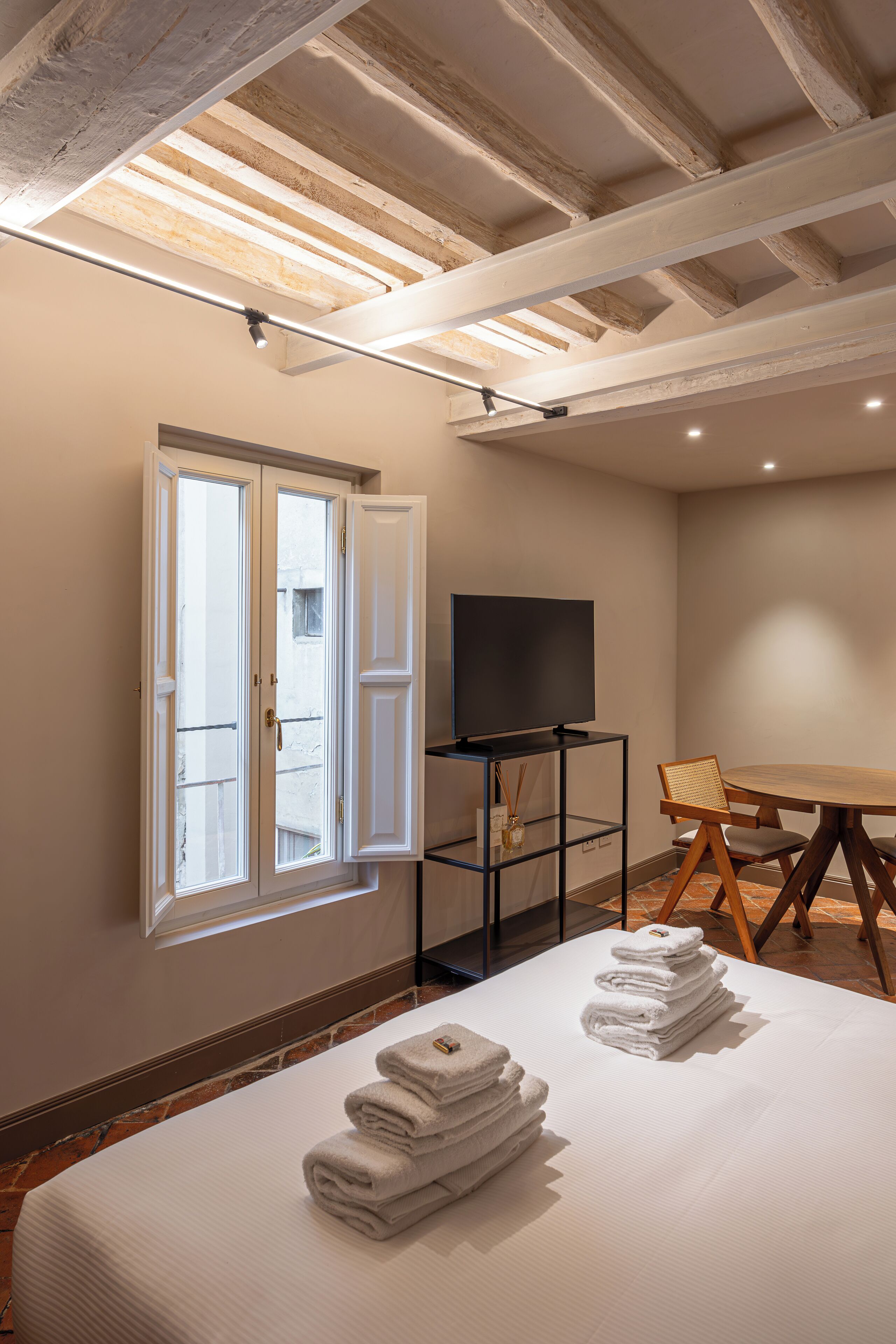 A hotel room with a bed, a TV, a dining table, and a window.