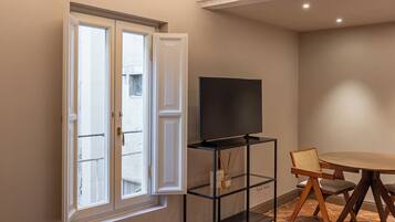 A hotel room with a bed, a TV, a dining table, and a window.