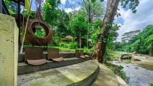 A stone staircase leading to a thatched-roof structure, surrounded by lush greenery and a flowing stream. - Jungle River Villa for 10 |Pool, ATV, Tubing| Ubud (Sukawati)