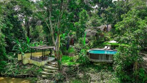 A lush, tropical resort with a swimming pool, a covered seating area, and a natural setting with dense vegetation. - Jungle River Villa for 10 |Pool, ATV, Tubing| Ubud (Sukawati)