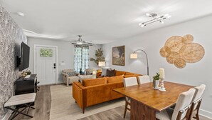 A modern living room with a wooden dining table, a sofa, and a TV on a stand. - Modern 4BR Retreat near Downtown Concord (Concord)