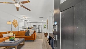 A modern kitchen with stainless steel appliances, a dining area with a wooden table and orange sofa, and a ceiling fan. - Modern 4BR Retreat near Downtown Concord (Concord)