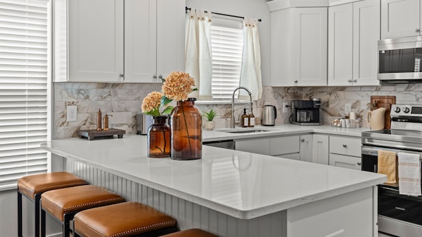 A modern kitchen with white cabinets, a marble backsplash, and stainless steel appliances. There are two stools at the island and a coffee maker on the counter. - Modern 4BR Retreat near Downtown Concord (Concord)