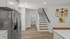 A kitchen with a stainless steel refrigerator, wooden flooring, white cabinetry, and a staircase leading to another level. - Modern 4BR Retreat near Downtown Concord (Concord)