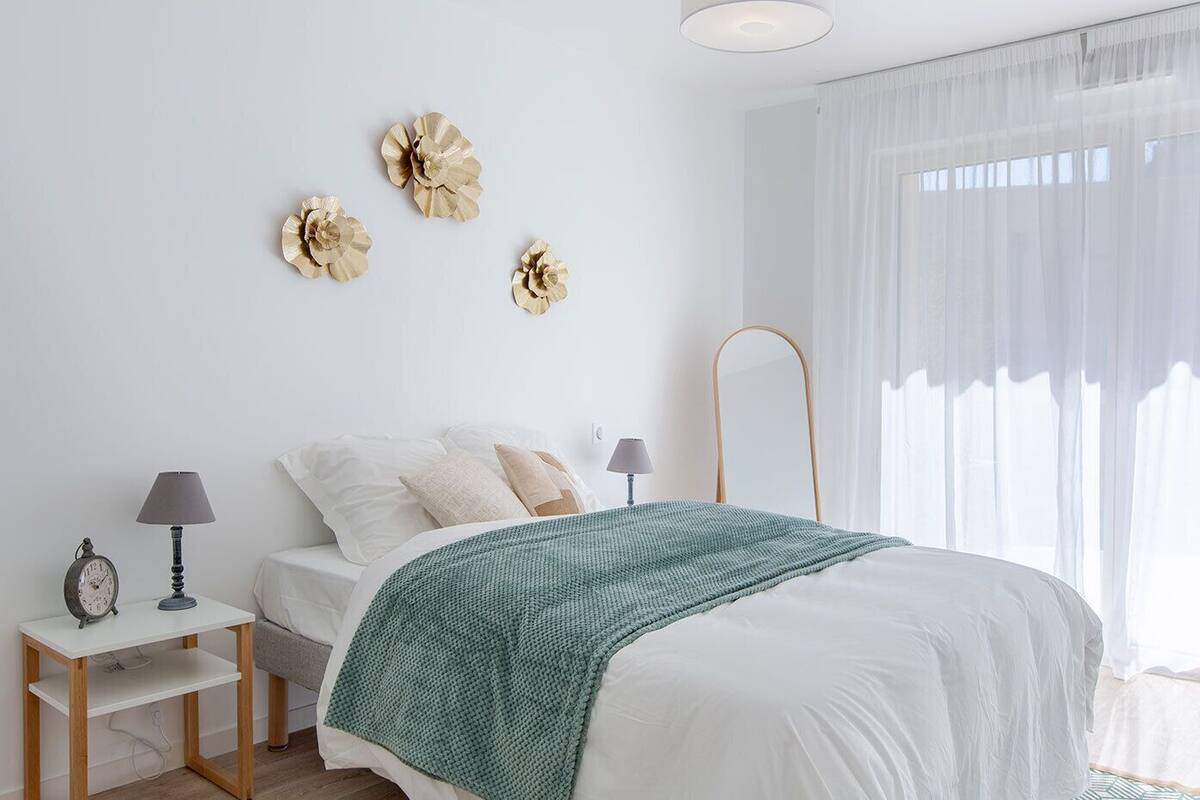 A bedroom with a bed, bedside tables, lamps, a clock, and decorative wall pieces.