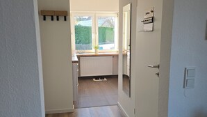 Un couloir menant à une cuisine équipée d’une fenêtre, d’un radiateur et d’une porte sur laquelle est fixé un porte-serviettes.
