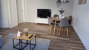 Un salon moderne comprenant un téléviseur à écran plat, une table à manger avec des chaises, une petite table basse et un canapé.