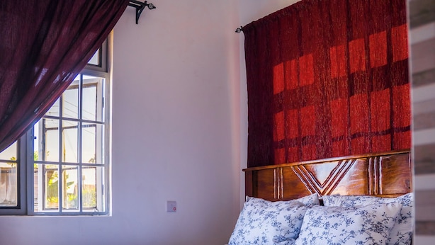 A bedroom with a wooden bed, a window with curtains, and a red headboard. - Osim bnb (Arusha)