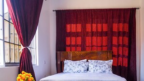 A bedroom with a wooden bed, a small round table with chairs, a window with curtains, and a vase of flowers. - Osim bnb (Arusha)