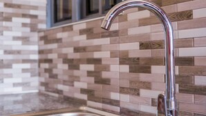 A kitchen with a stainless steel sink, a modern faucet, and a tiled backsplash. - Osim bnb (Arusha)