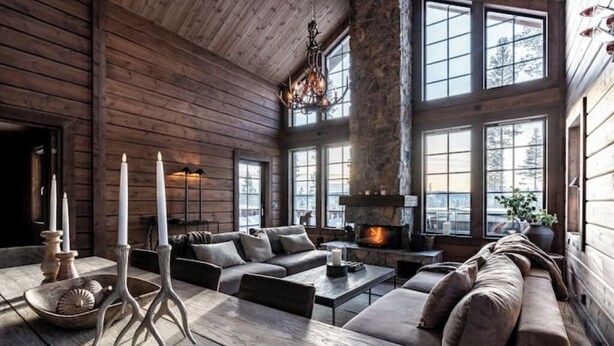 Un intérieur chaleureux de chalet en bois avec une cheminée, de grandes fenêtres et un salon moderne.