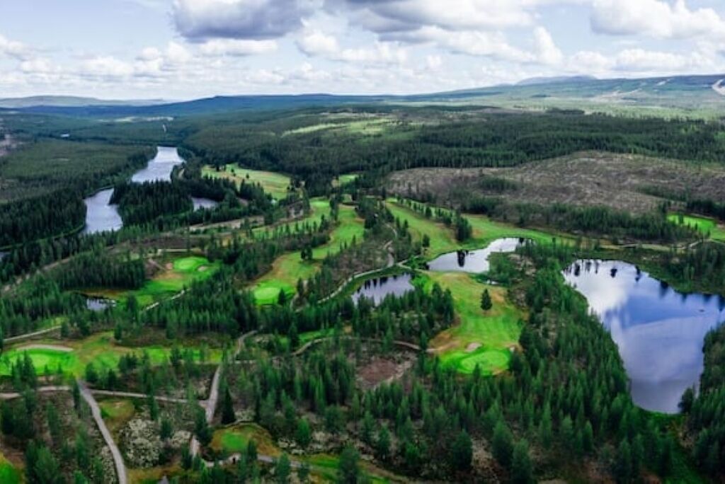 A panoramic view of a golf course with multiple ponds and dense forests.