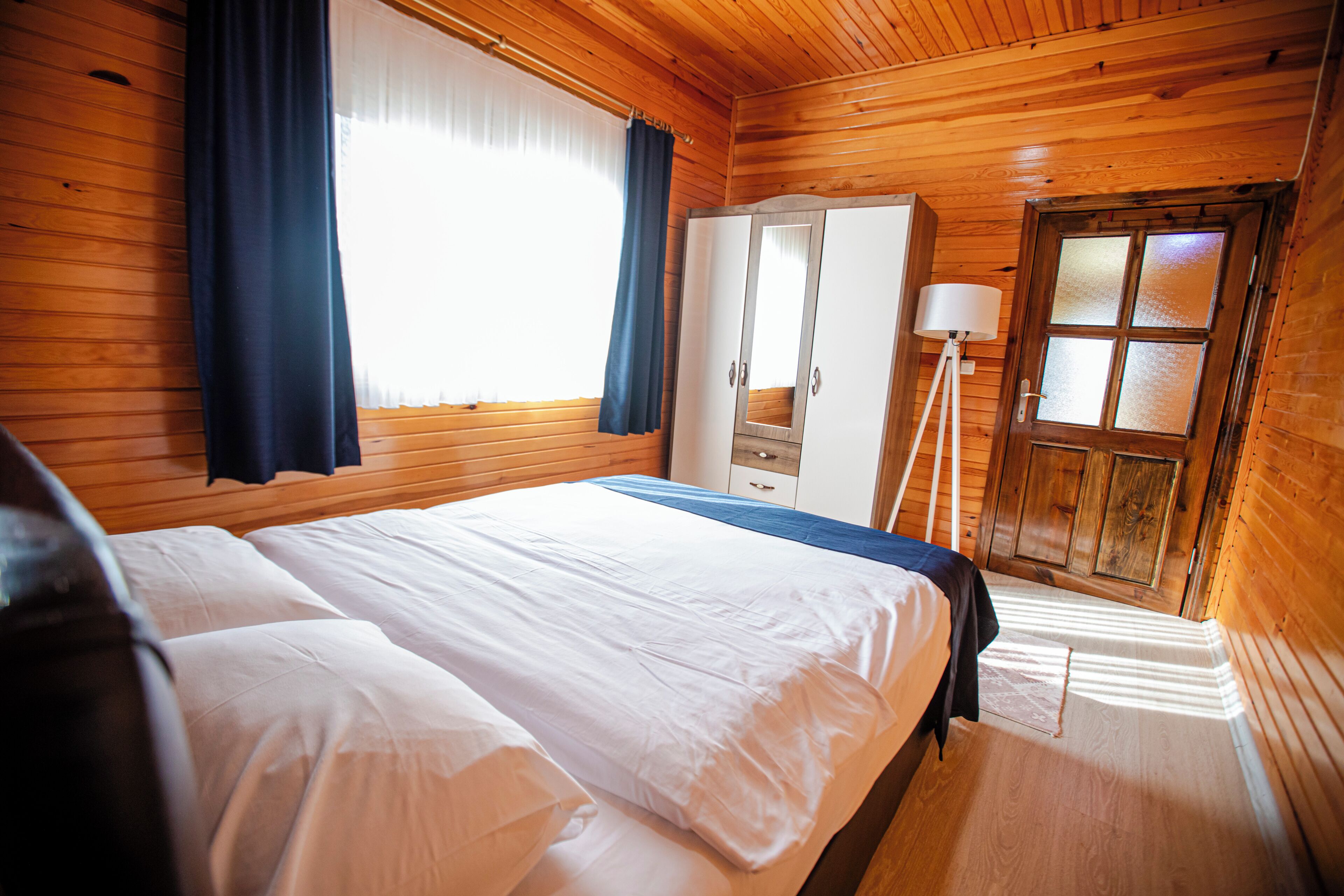 Une chambre dans une cabane en bois, avec un grand lit, une armoire et une fenêtre avec des rideaux.