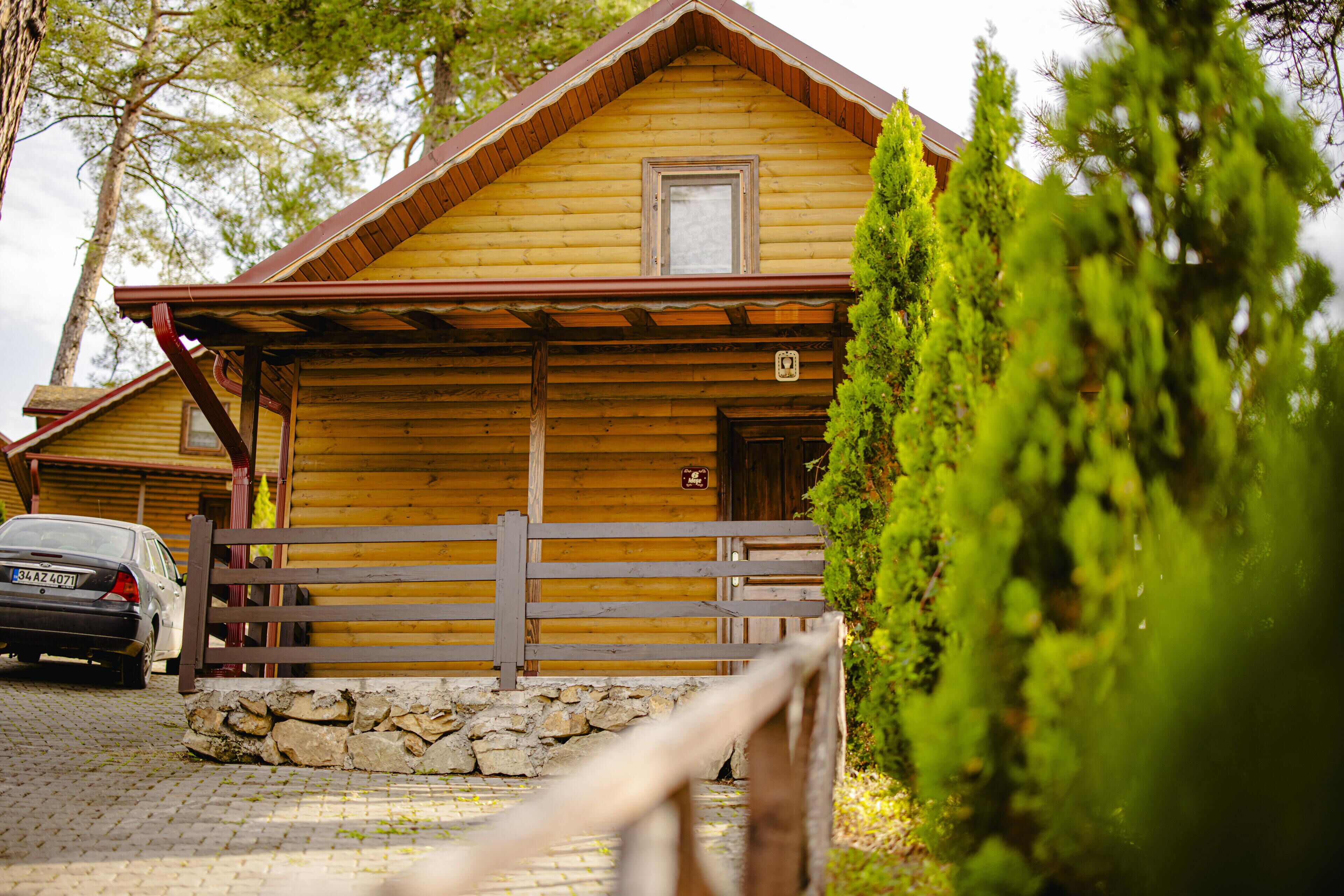 A wooden cabin with a stone foundation, a wooden porch, and a car parked in front.