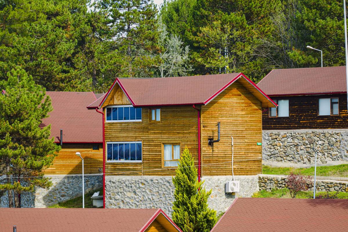 A wooden cabin with a stone foundation, multiple windows, and a red roof.