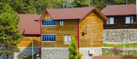 A wooden cabin with a stone foundation, multiple windows, and a red roof.