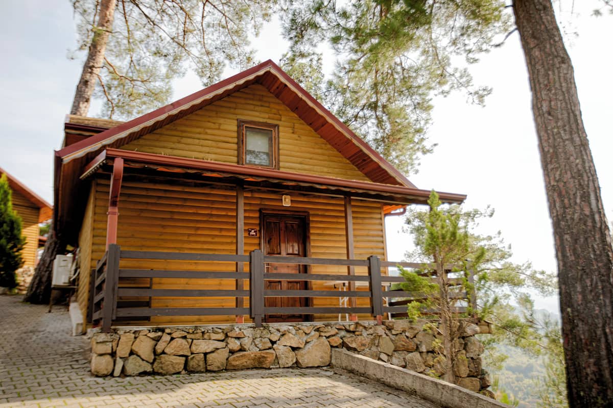 A wooden cabin with a stone foundation, a wooden porch, and a wooden fence.