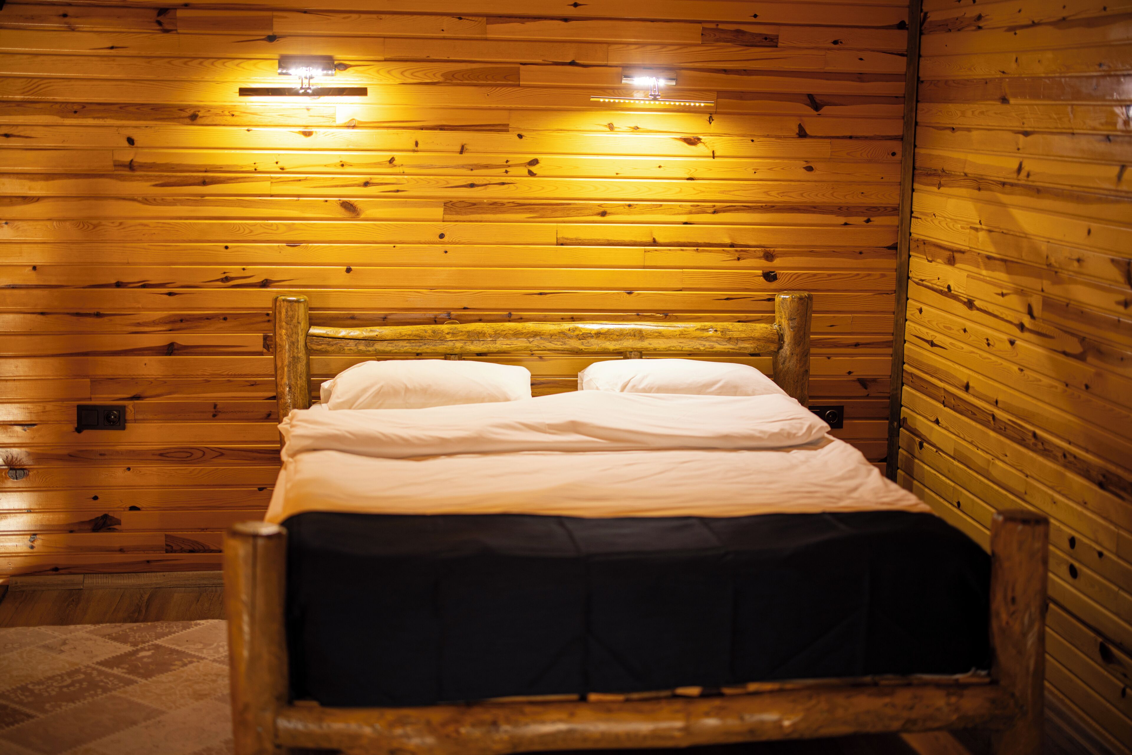 A wooden cabin-style room with a bed, two wall-mounted lights, and a wooden headboard.