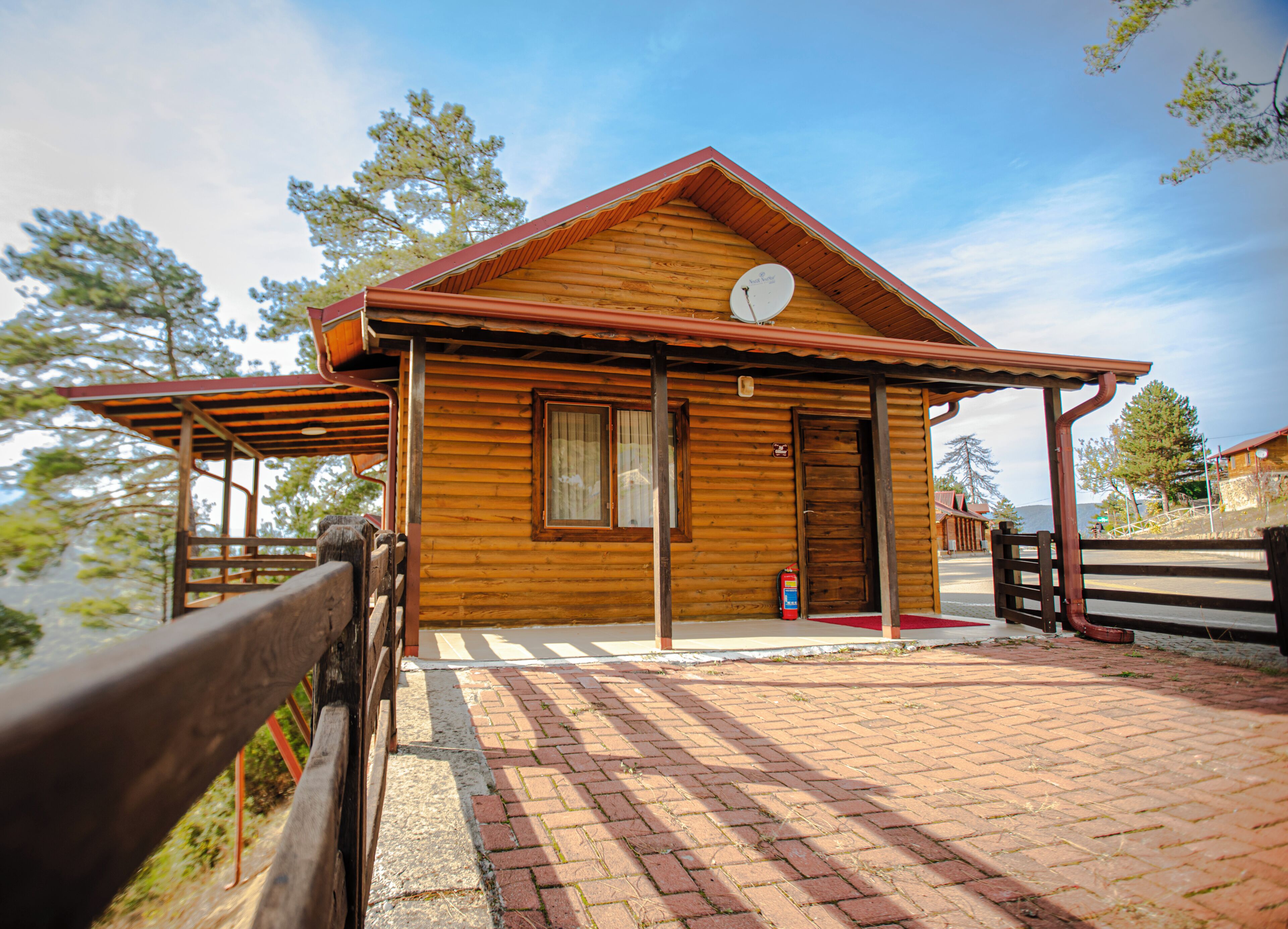 A wooden cabin with a red roof, a satellite dish, and a brick-paved entrance.