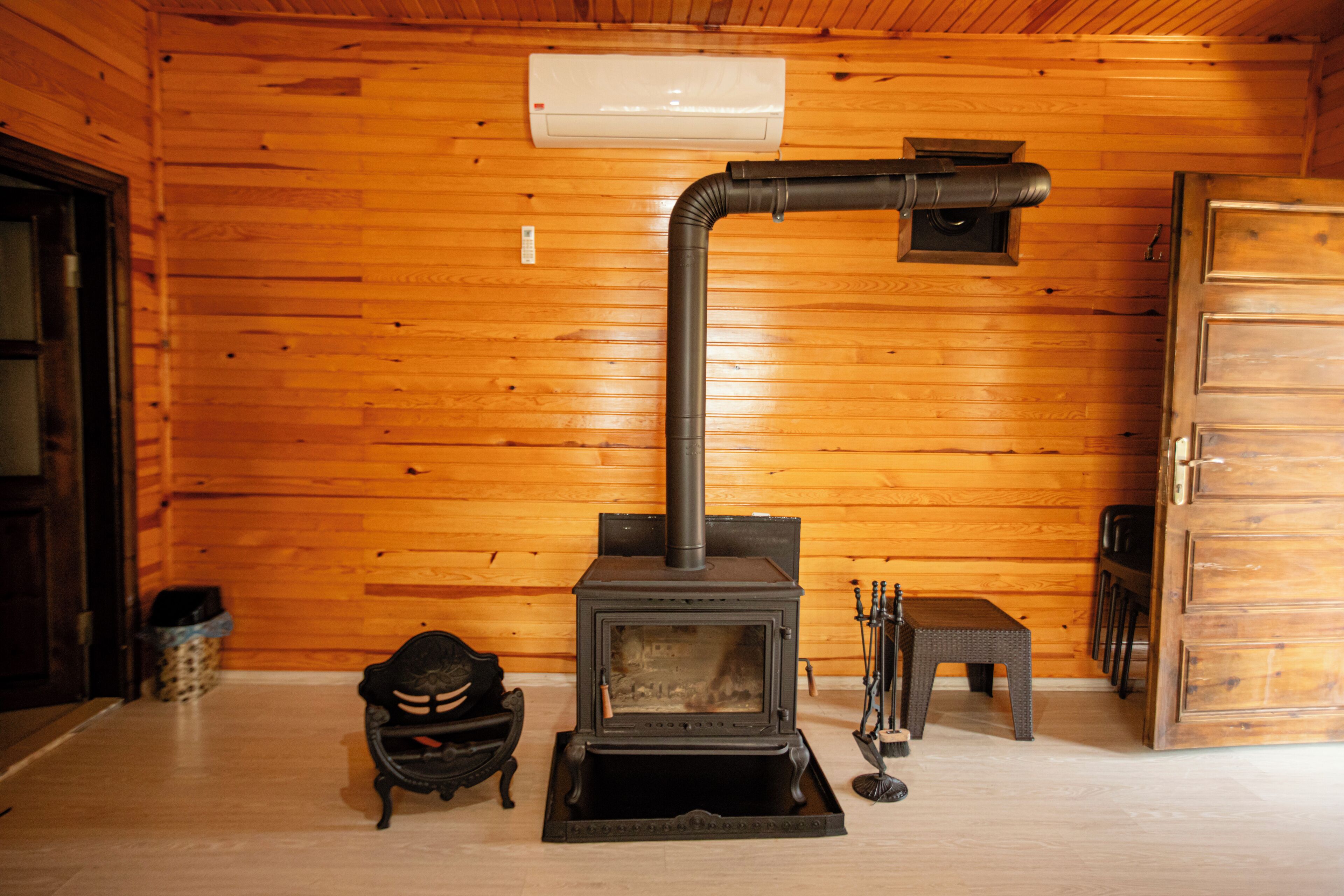 A wooden cabin interior with a wood-burning stove, a bench, and a door.
