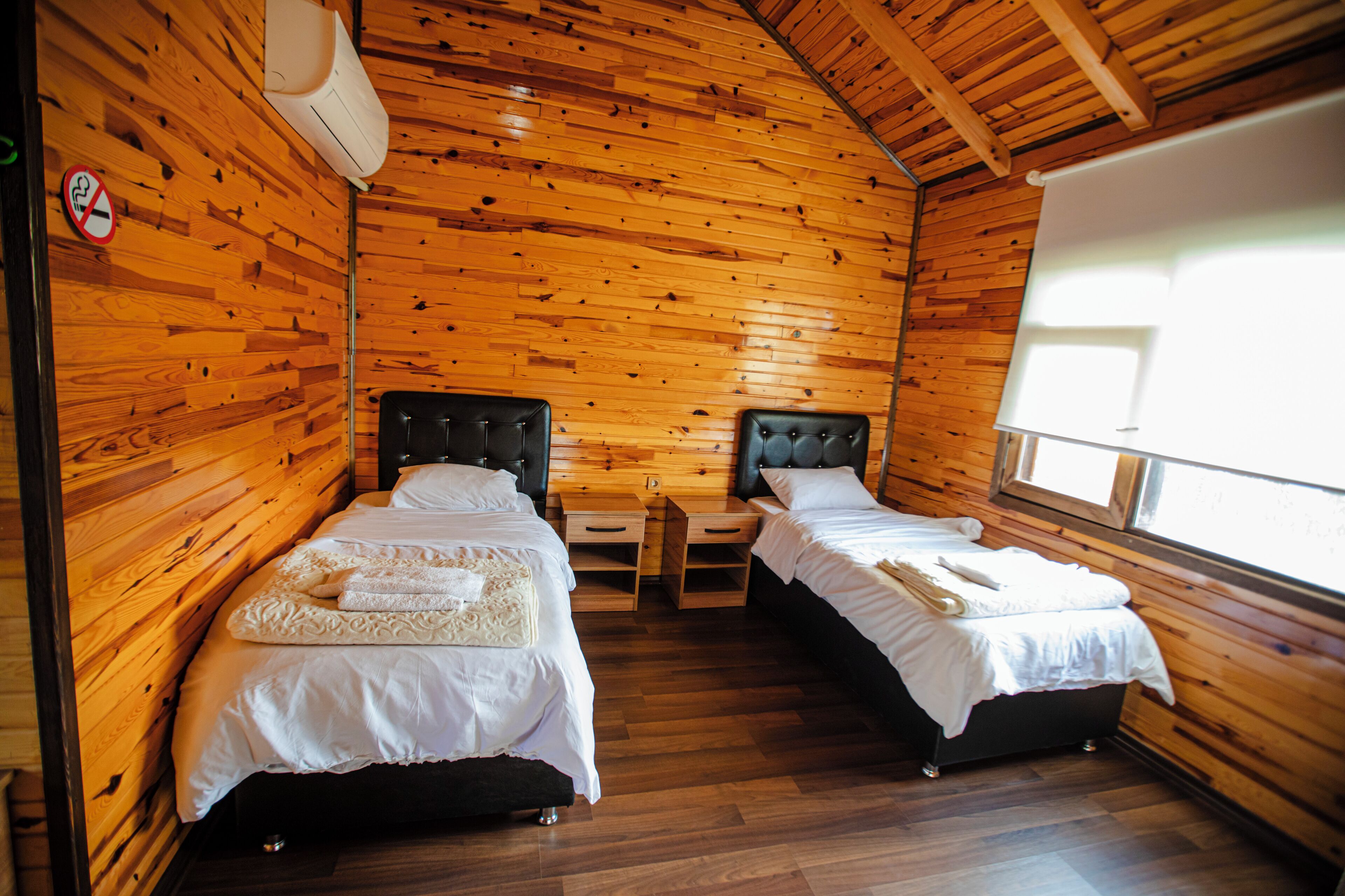 A wooden cabin room with two beds, a window, and a no-smoking sign.