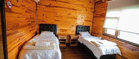 A wooden cabin room with two beds, a window, and a no-smoking sign.