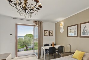 A modern bedroom with a balcony, a dining area, and a view of the sea. - Panoramic Apartment with Lake View, Wi-Fi, Air Conditioning & Private Parking (Padenghe Sul Garda)
