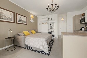 A modern bedroom with a bed, bedside table, lamp, and a chandelier. - Panoramic Apartment with Lake View, Wi-Fi, Air Conditioning & Private Parking (Padenghe Sul Garda)