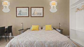 A bedroom with a large bed, two bedside lamps, a desk with a chair, and two framed pictures on the wall.