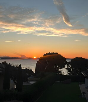 A sunset over a coastal landscape with a prominent rock formation silhouetted against the sky. - Panoramic Apartment with Lake View, Wi-Fi, Air Conditioning & Private Parking (Padenghe Sul Garda)