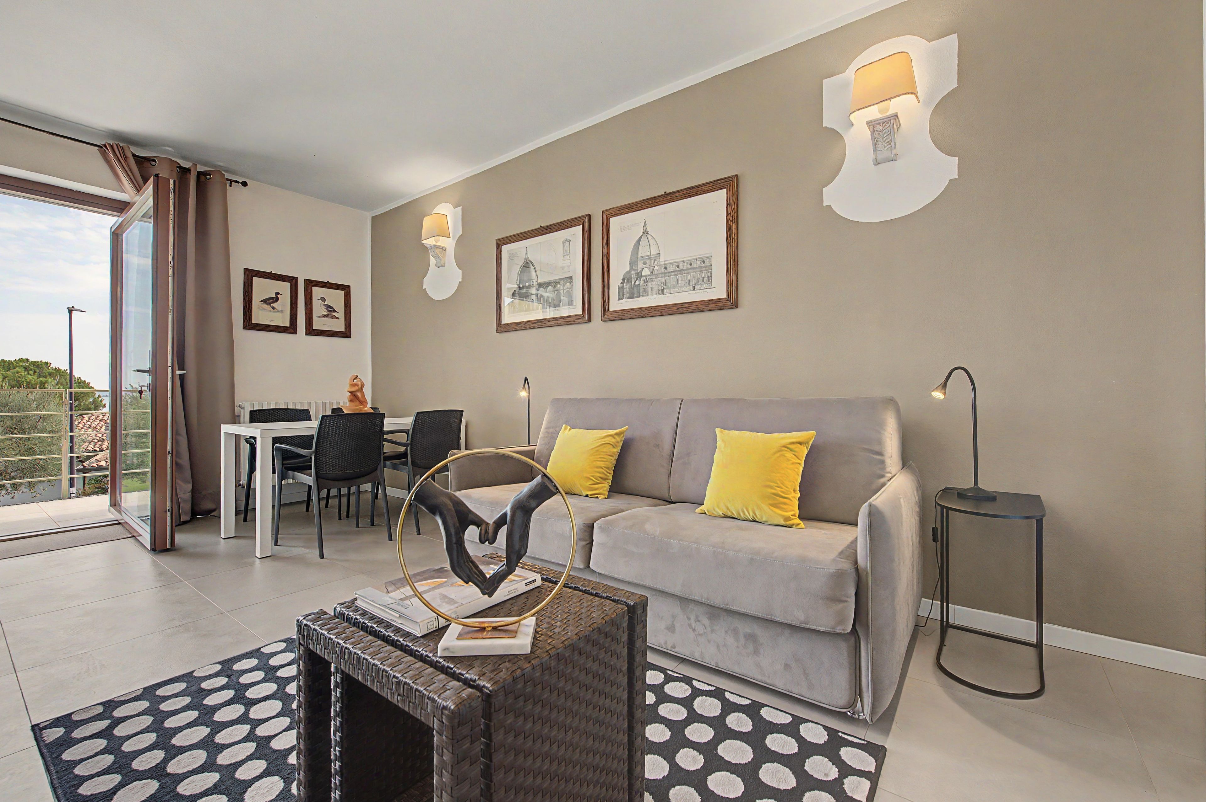 Una sala moderna con un sofá gris, cojines amarillos, una mesa de comedor con sillas y obras de arte en las paredes.
