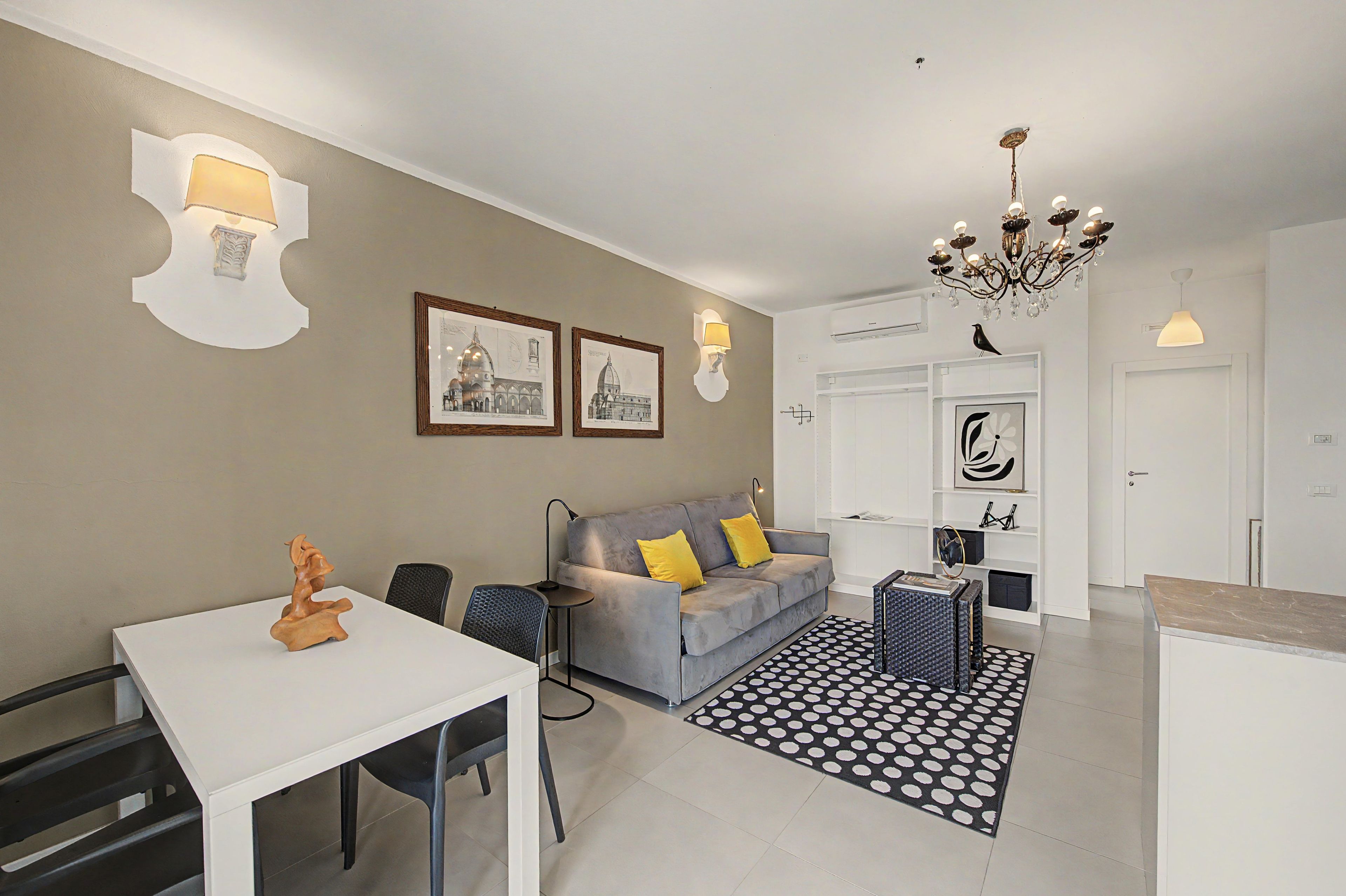 A modern living room with a grey sofa, a white dining table, and a black and white patterned rug.