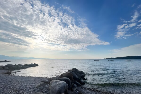 A rocky shoreline with calm water, boats, and a clear sky.