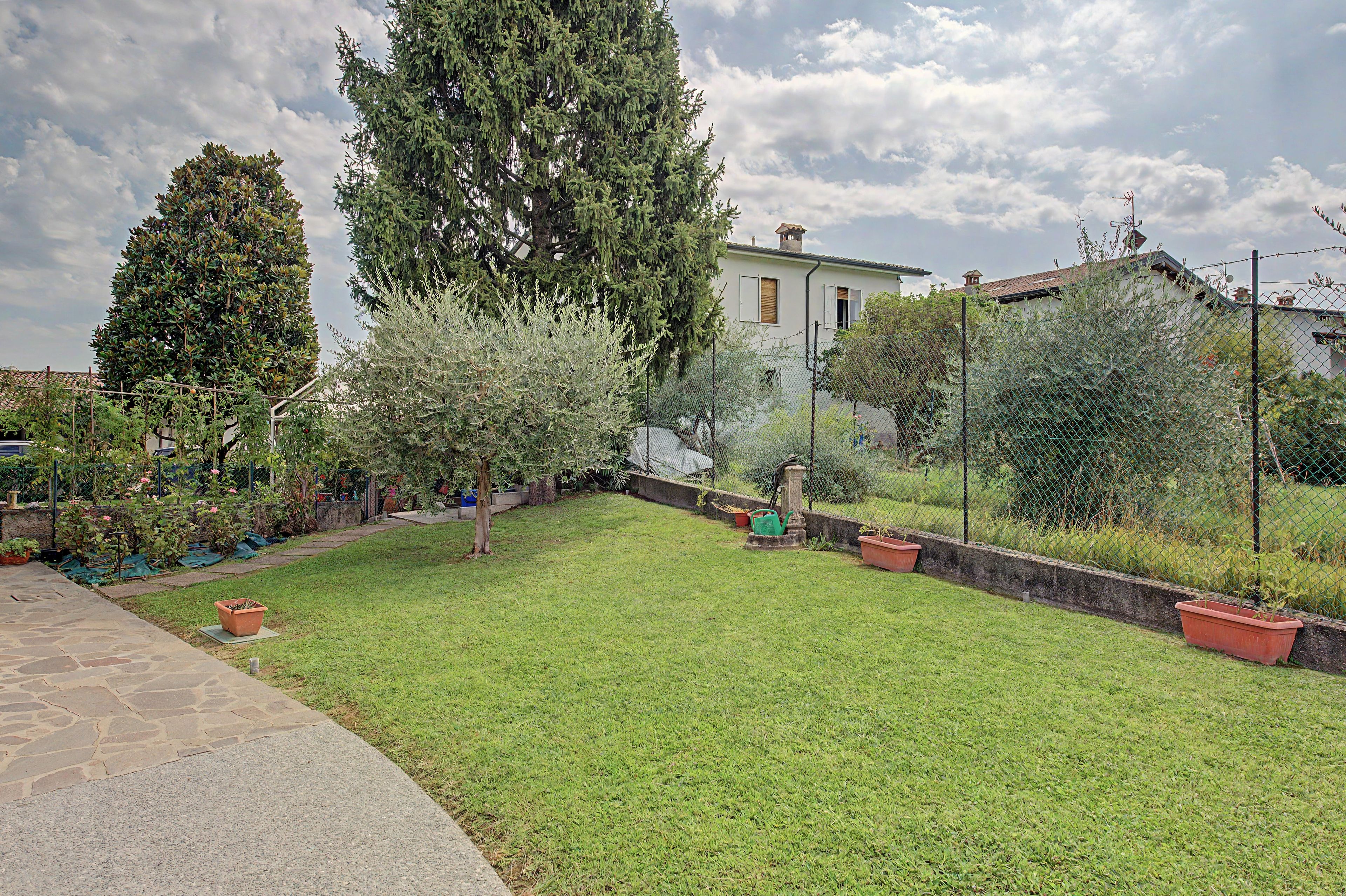 Un jardin bien entretenu, agrémenté de divers arbres et arbustes, un chemin pavé et une zone délimitée par une clôture.