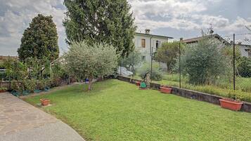 Un jardín bien cuidado con diversos árboles y arbustos, un sendero pavimentado y una zona cercada.