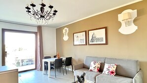 Un saló modern amb un sofà gris, una làmpada de cristall, una zona de menjador i una catifa amb dibuixos.