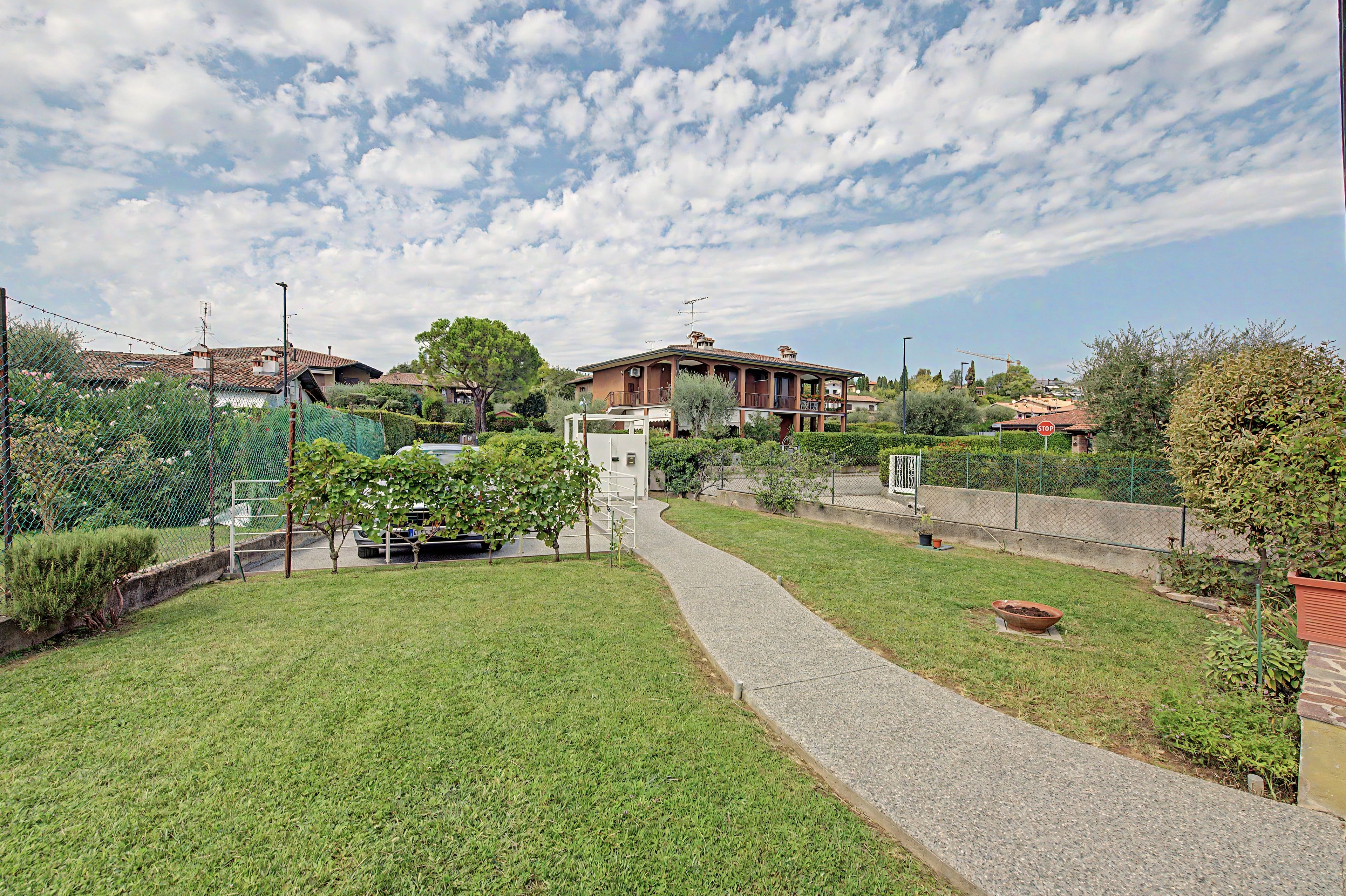 A residential area with a paved pathway, greenery, and houses.
