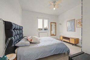 Un dormitorio con cama, lámpara de noche, cómoda y ventilador de techo.