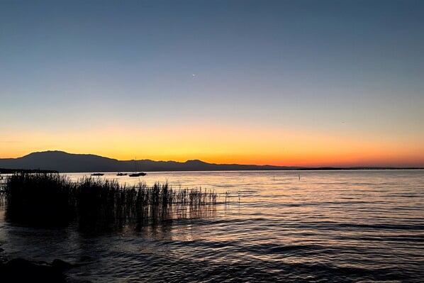 A calm body of water with a distant mountain range and a clear sky. - Panoramic Apartment with Lake View, Wi-Fi, Air Conditioning & Private Parking (Padenghe Sul Garda)