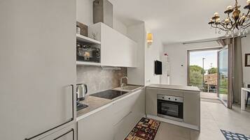 A modern kitchen with white cabinetry, a built-in oven, and a coffee machine.
