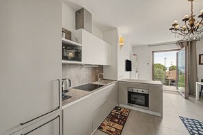 Una cocina moderna con armarios blancos, horno integrado y cafetera.