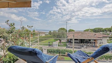 Un balcone con due poltrone e una vista aperta su una zona residenziale, sotto un cielo parzialmente nuvoloso.