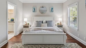 Een slaapkamer met een wit bed, twee nachtkastjes met lampen, een grote spiegel en kunstwerken aan de wanden.
