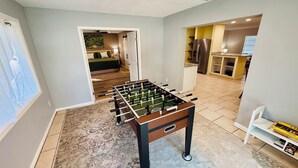Une pièce avec un baby-foot, un coin cuisine équipé d’un réfrigérateur et une bibliothèque contenant des jeux de société.