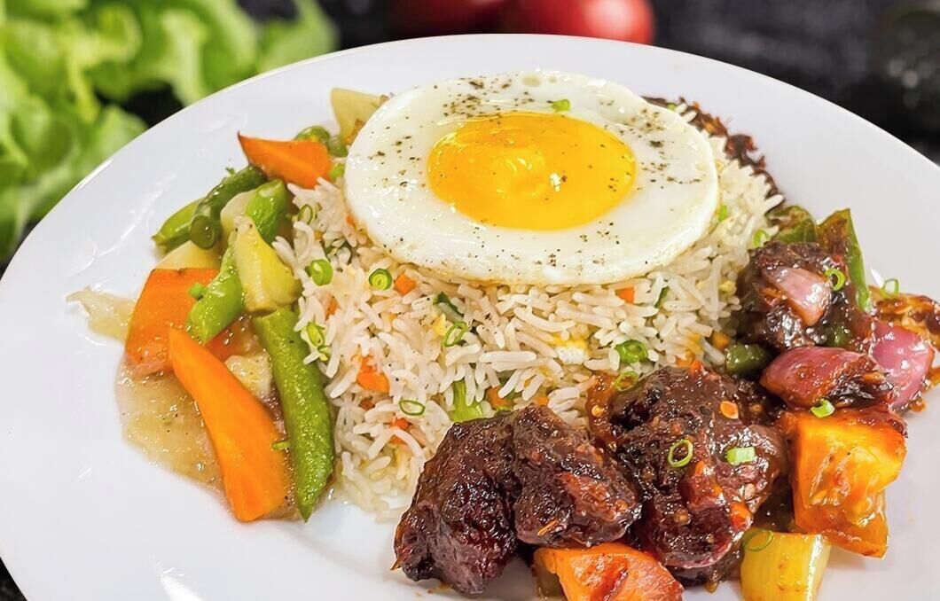Un plato de arroz frito con verduras y un huevo frito encima.